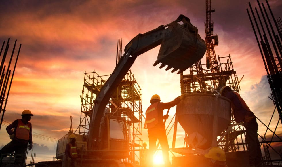 Contractor stands under excavator bucket as he cuts waste in construction