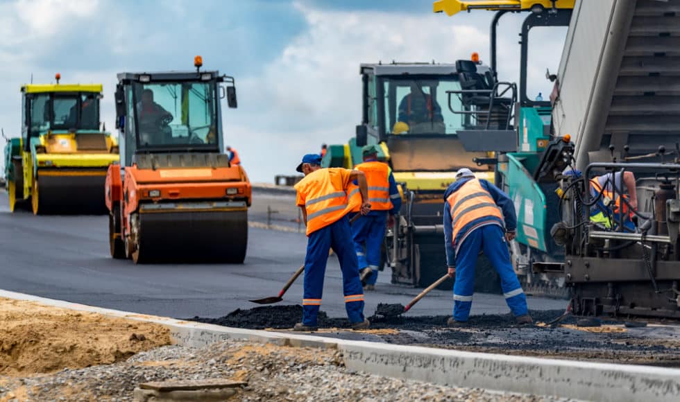 Workers build new road using modern asphalt paving systems.